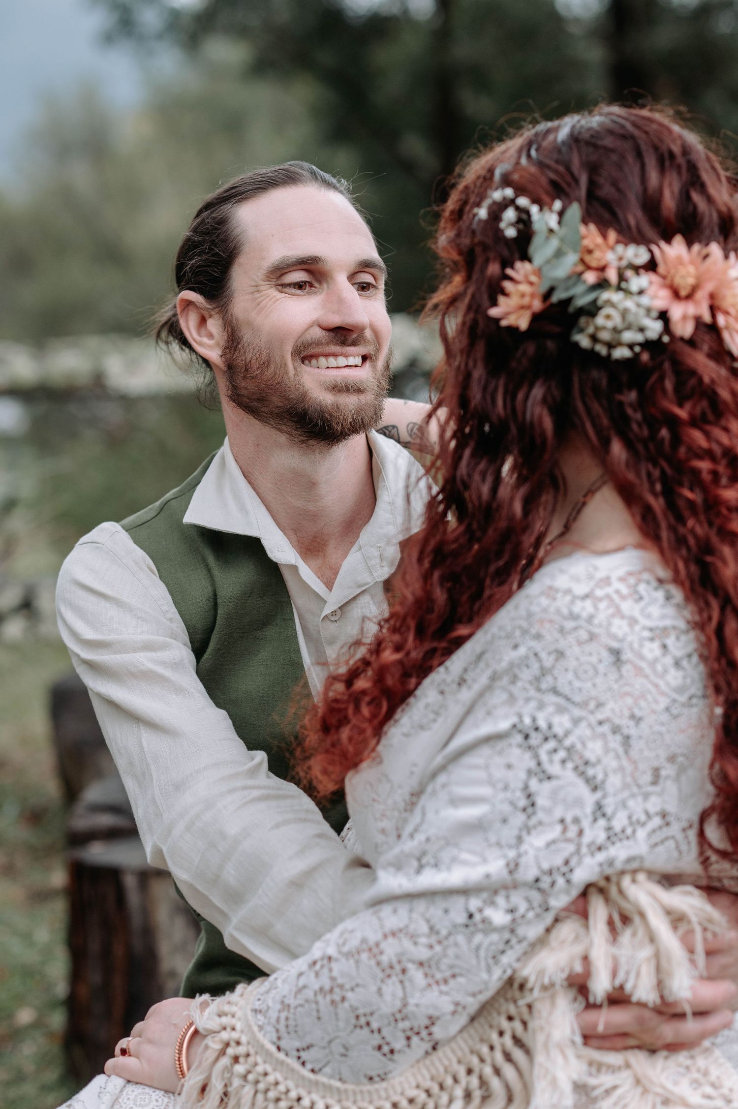 A romantic wedding couple shares a tender moment outdoors, with dried flowers adorning the bride's hair.