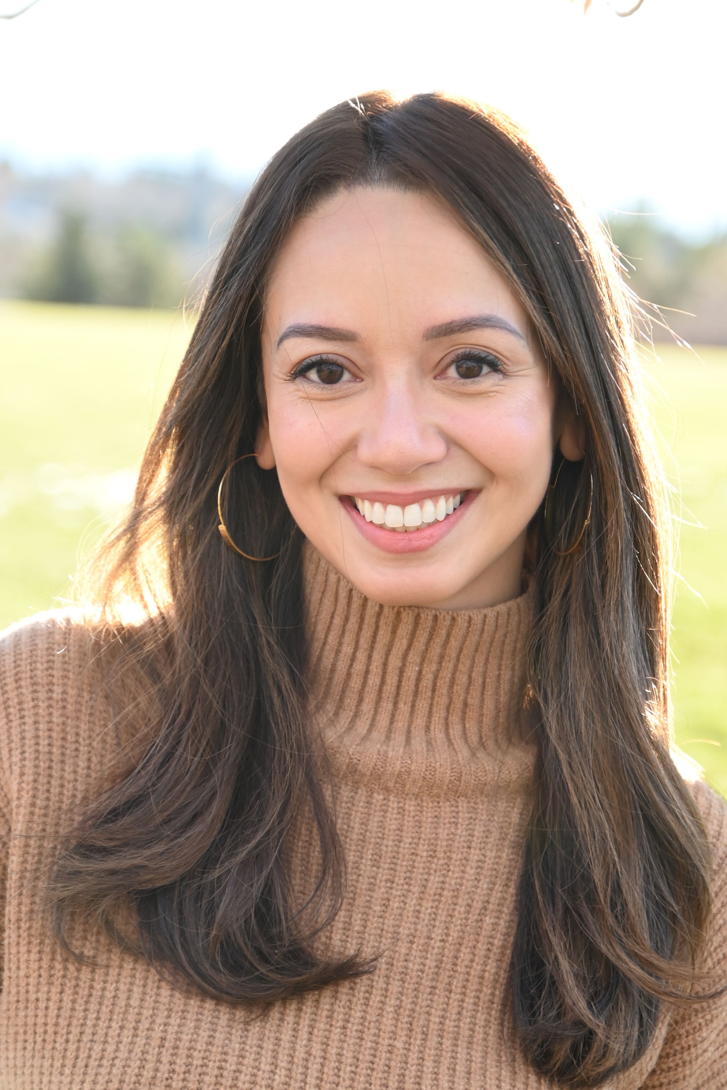 A person in a brown turtleneck sweater smiles warmly in a series of four photos with a sun-lit field in the background.