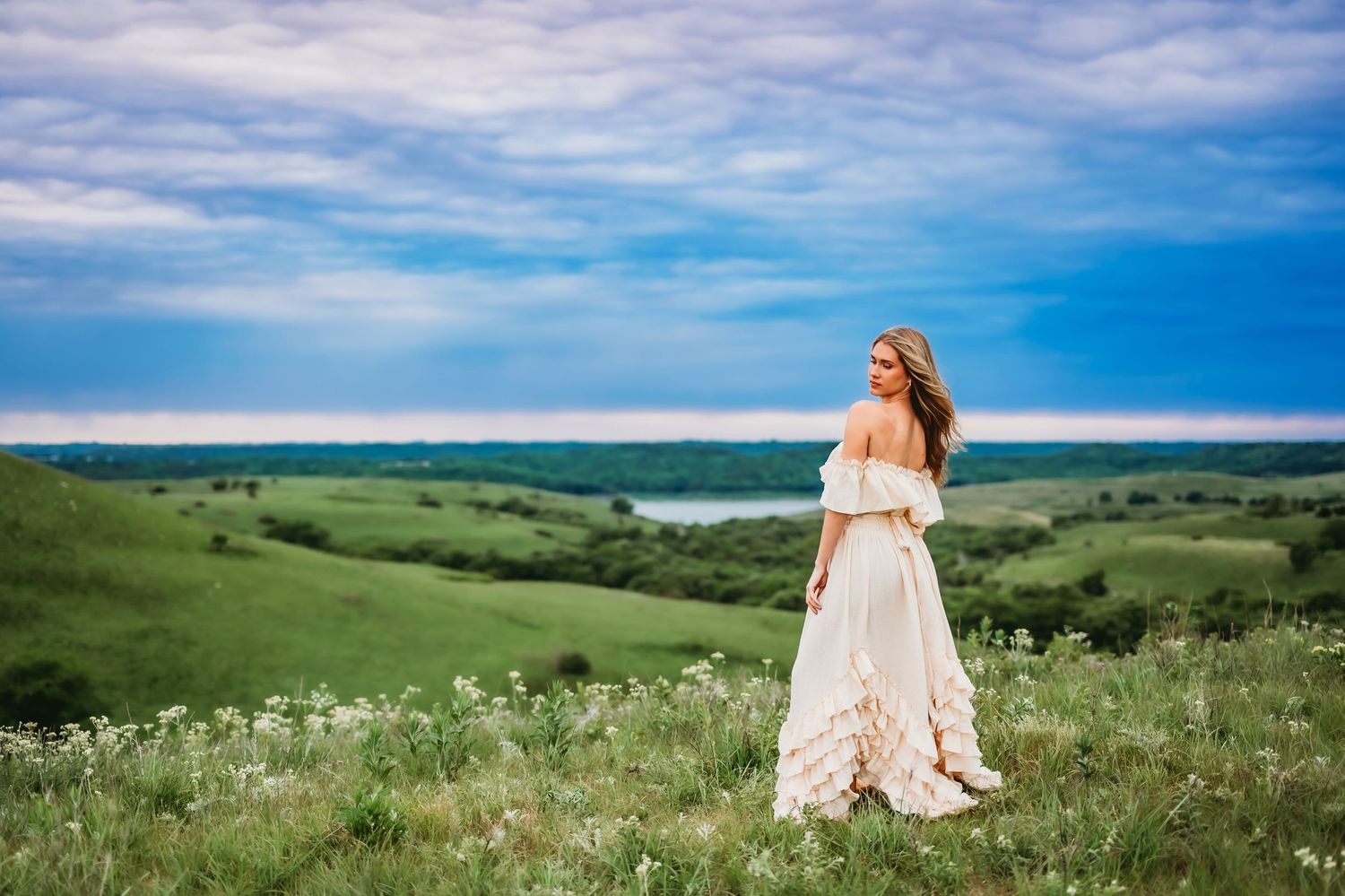 A scenic panoramic view of rolling green hills and vibrant wildflowers under a bright blue summer sky.