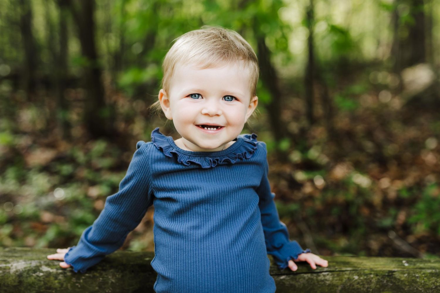 Smiling toddler in blue sweater plays outdoors among fallen autumn leaves.