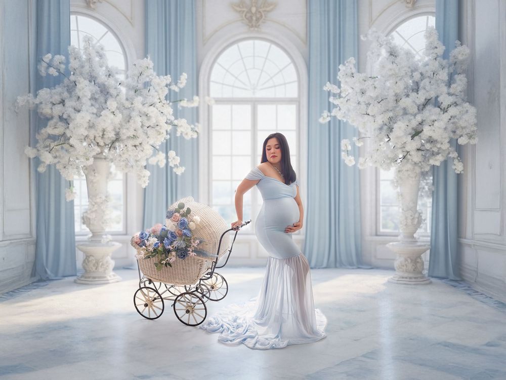 Dreamy maternity photoshoot in a blue and white room with vintage baby carriages and floral arrangements.