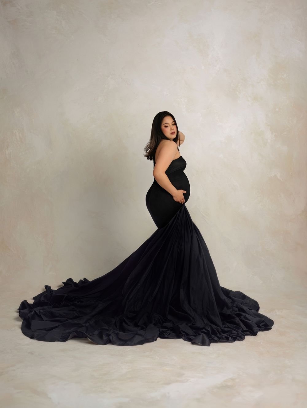 A flowing black formal gown with a dramatic train creates an elegant silhouette against a light neutral backdrop.