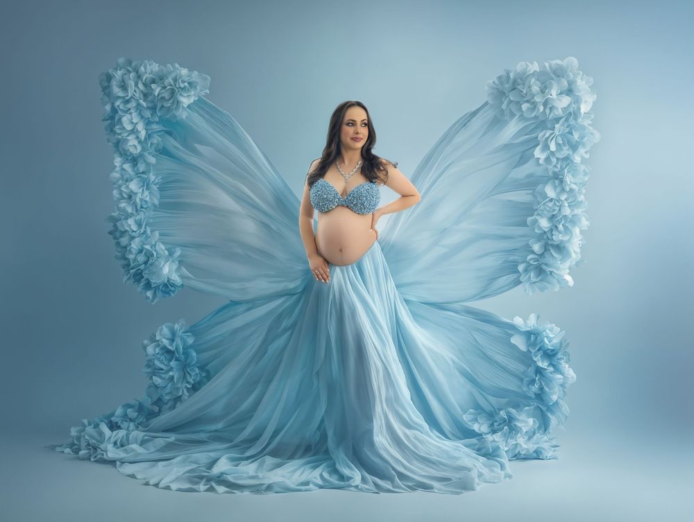 A feminine figure in a flowing pastel blue gown poses gracefully against a dreamy light blue studio backdrop.
