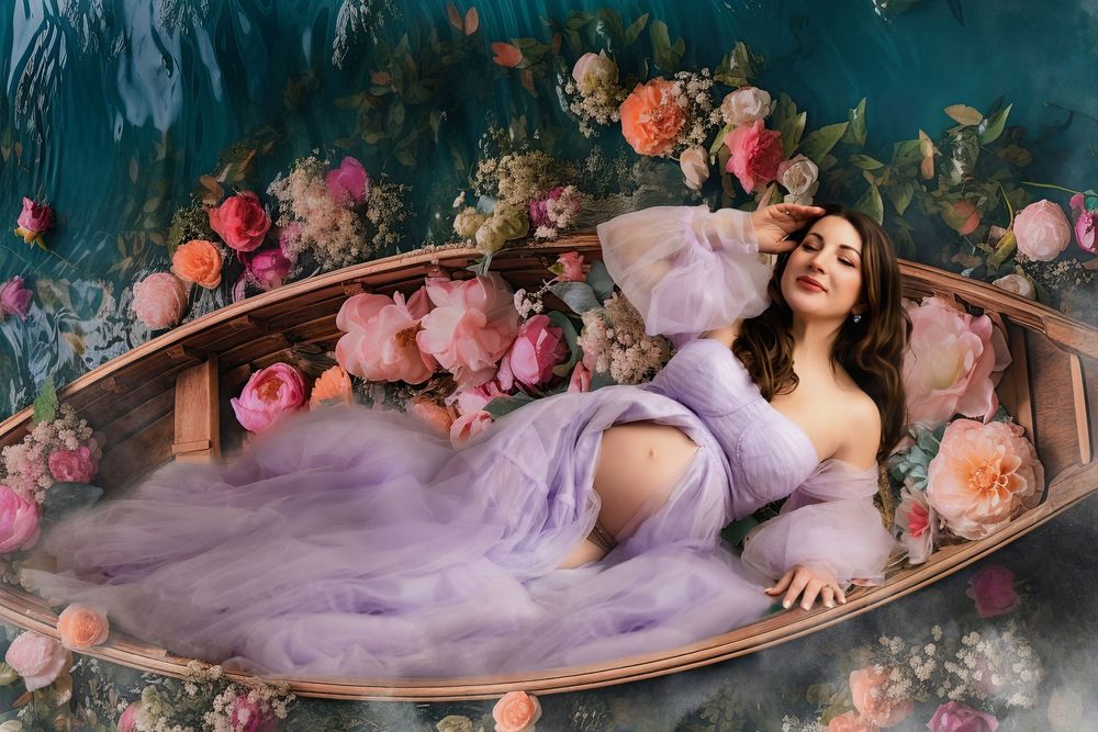 Dreamy maternity photoshoot with a woman in a flowing lavender dress surrounded by pink and peach flowers.
