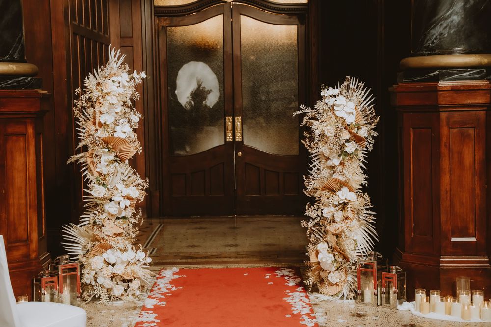 Elegant wedding ceremony entrance with white feather-adorned pillars and glowing candles lining a red carpet aisle.