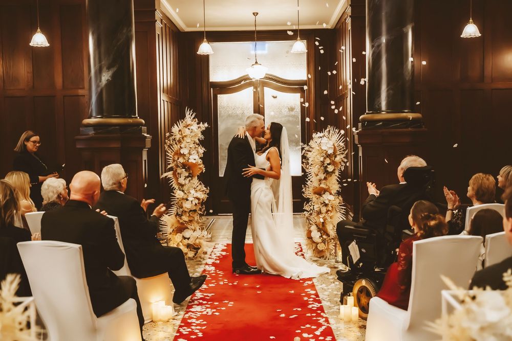 Reception hall decorated with formal table settings, white chairs, and elegant floral centerpieces.