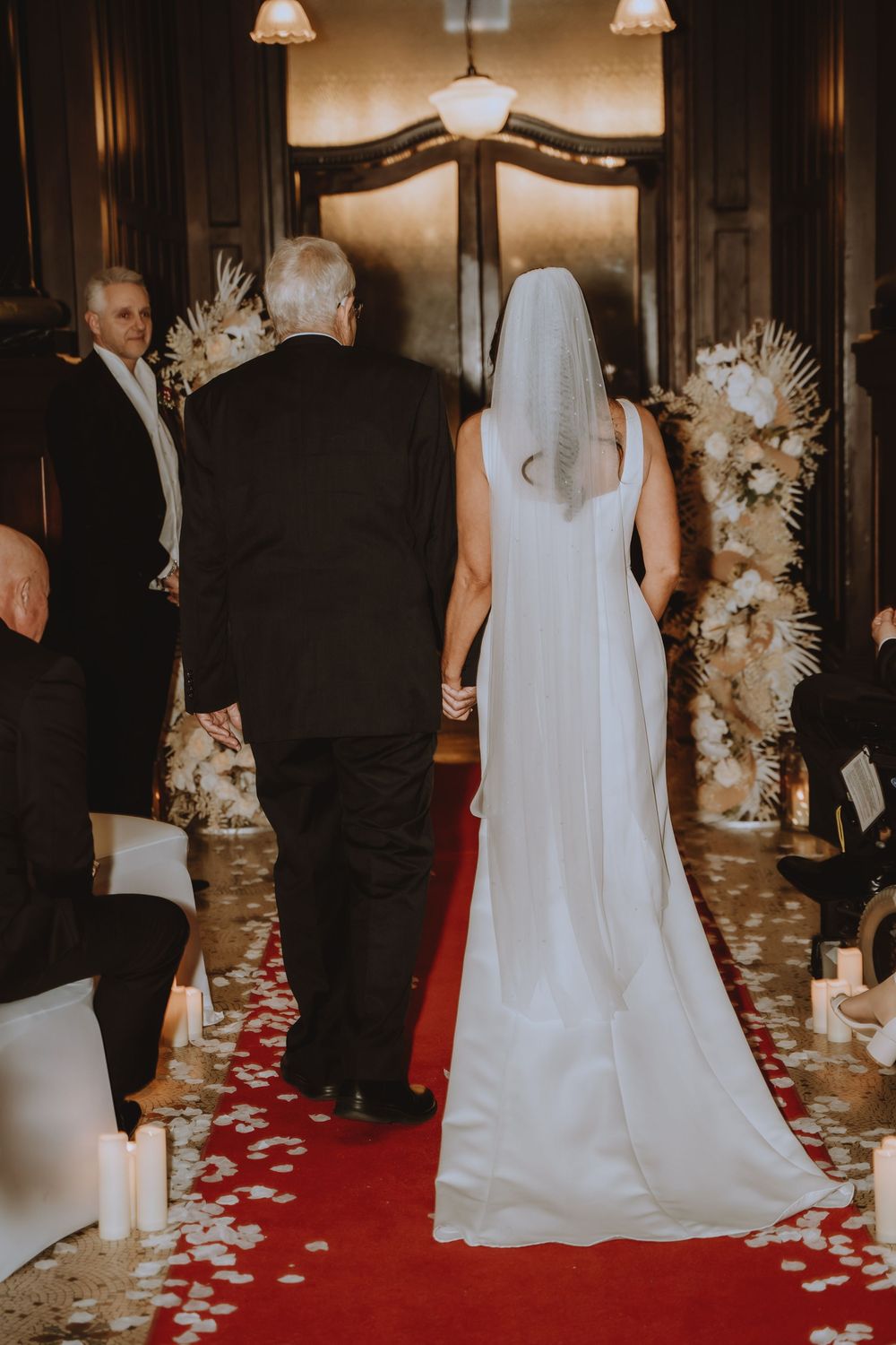 Wedding ceremony setup with elegant red carpet aisle runner decorated with white rose petals and floral arrangements.