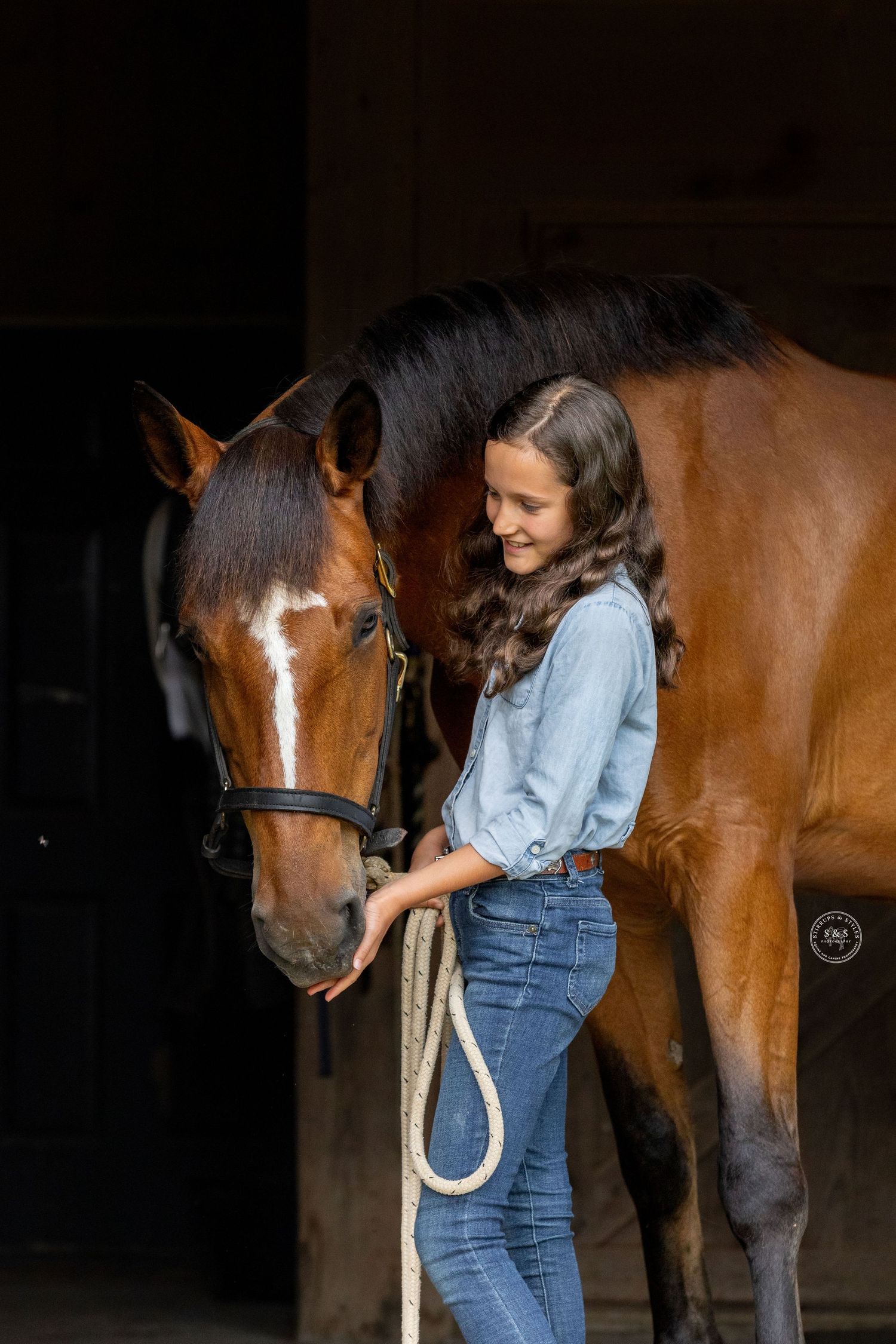 A majestic brown horse and person in a white dress share a tender moment in a sunlit meadow at golden hour.