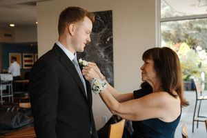 A person helps adjust a light blue bow tie on a groom wearing a black suit during wedding preparations.