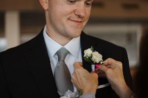 A close-up series of someone adjusting a gray necktie and white floral boutonniere against a dark suit.