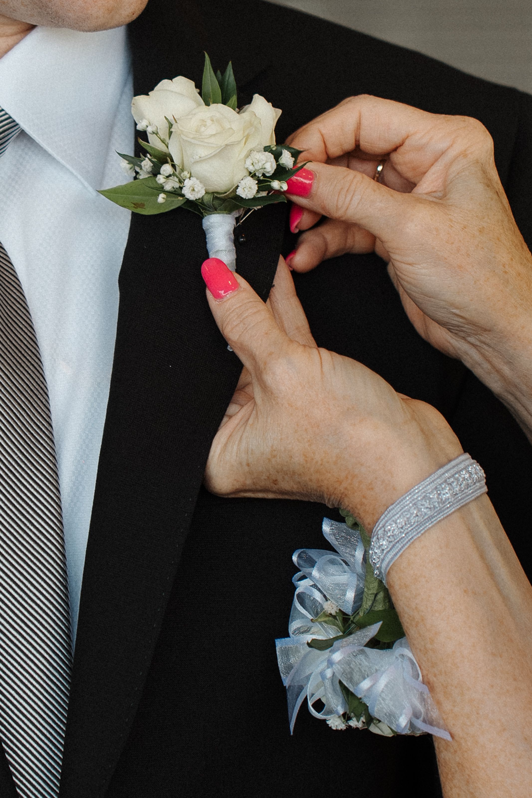 Hands carefully pin a white rose boutonniere with small flowers and gray ribbon to a lapel in sequential steps.
