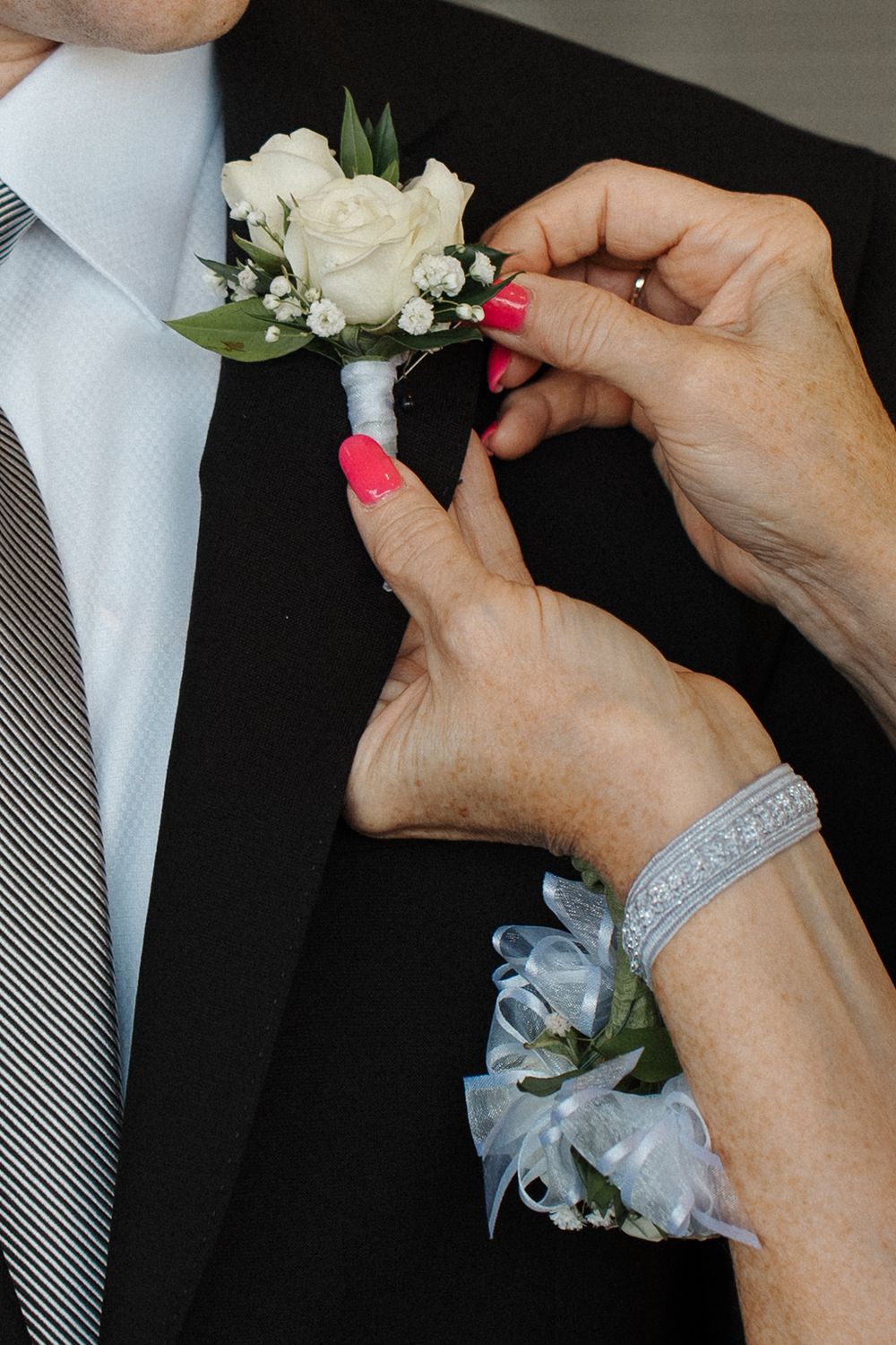Hands carefully pin a white rose boutonniere with small flowers and gray ribbon to a lapel in sequential steps.