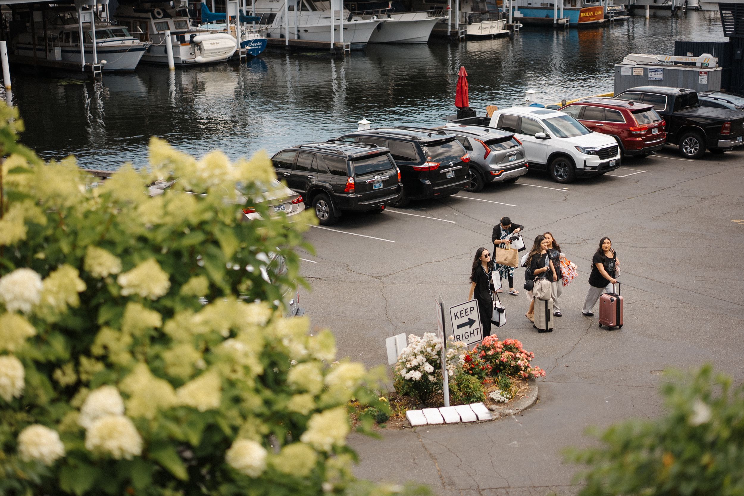 Waterfront marina with boats docked alongside a parking area on a cloudy day.