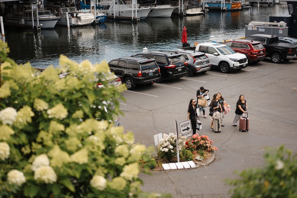 Waterfront marina with boats docked alongside a parking area on a cloudy day.