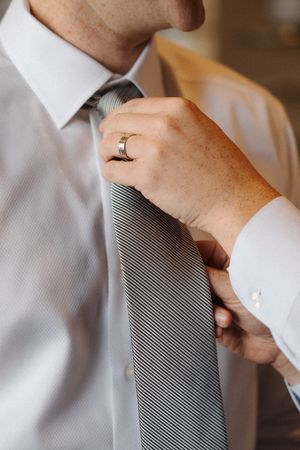 Close-up of someone adjusting a gray striped necktie against white shirt collar in natural lighting.