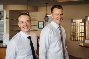 Two people in white button-down shirts share a laugh in an office setting.