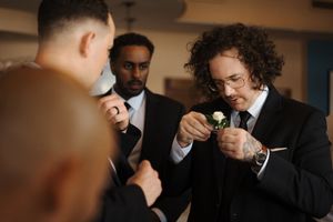 Groomsmen in formal suits stand together lighting cigars before a wedding celebration.