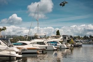 Row of boats and yachts docked at a marina on a sunny day with blue skies and white puffy clouds.
