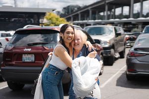 A couple in casual attire shares a joyful laugh while standing in an outdoor parking area.