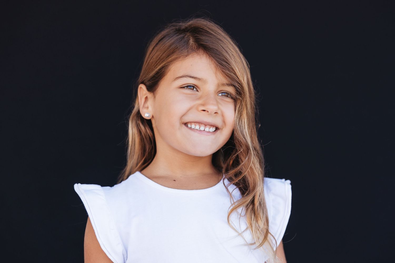 A joyful young child in a long sleeve shirt making a playful expression while holding their hands near their face in black and white.