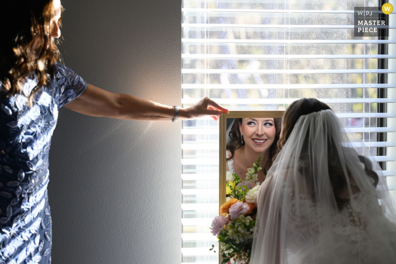 A short wedding veil with a dark bow accent hangs from a window blind in natural lighting.