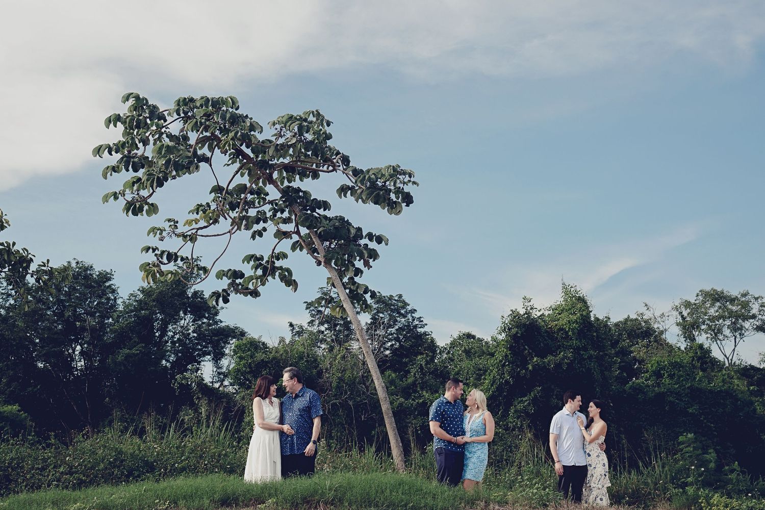 A family photo session in Playa del Carmen featuring Rachel and Sebastian Roldan with Sebastian's parents and brother under a tropical tree.