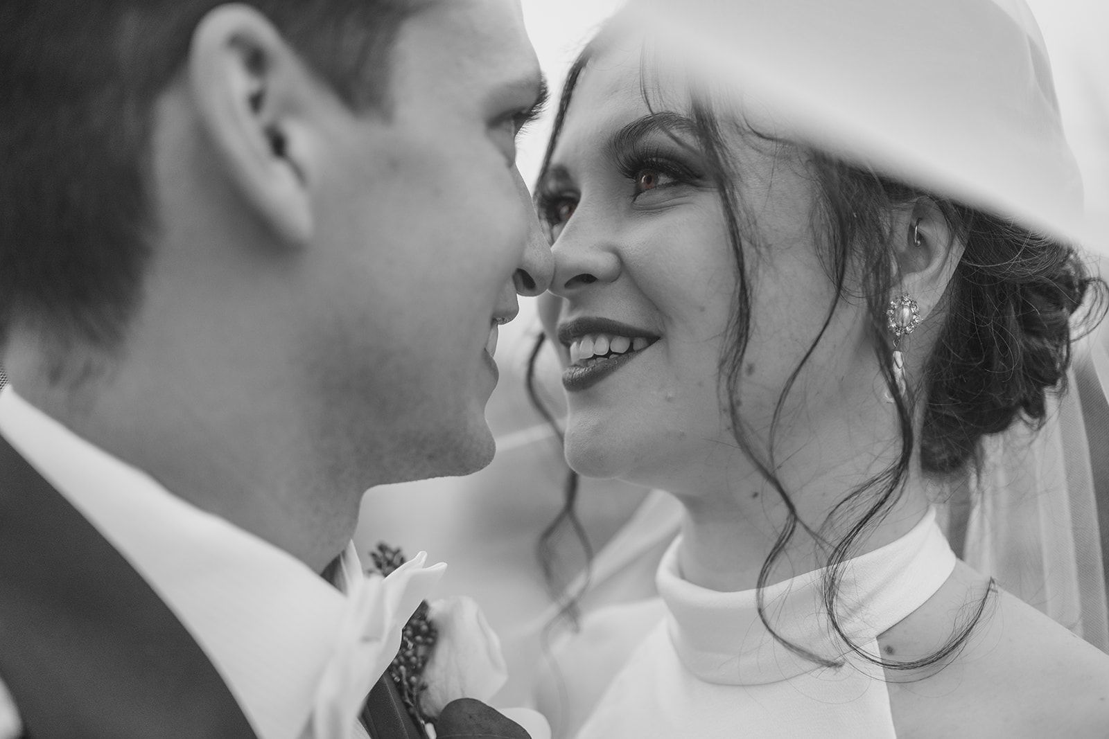 A black and white close-up of a joyful bride in a white dress and veil sharing an intimate moment with her groom.