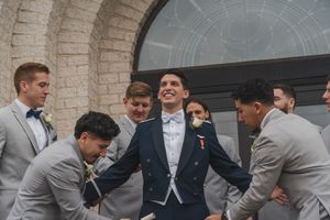 Wedding party in gray suits and bow ties sharing a candid laughing moment together.