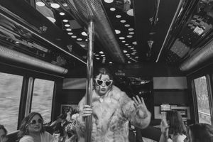 Party-goer in sunglasses dancing on a bus with festive lighting and other passengers visible.