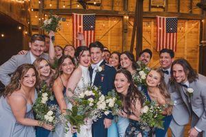 Wedding party gathered in rustic barn venue with American flags and natural decor in background.