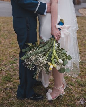 Detail shot of newlyweds' legs with bride holding rustic bouquet of baby's breath and greenery.