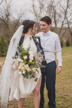 Bride holding elegant bouquet poses with groom in outdoor wedding portrait.