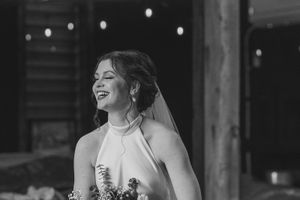 Black and white photo showing a joyful bride in a halter wedding dress laughing during a reception celebration.