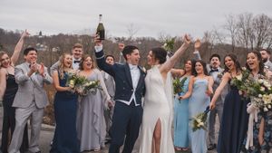 A wedding party celebrates outdoors with bridesmaids in blue dresses and groomsmen in gray suits.