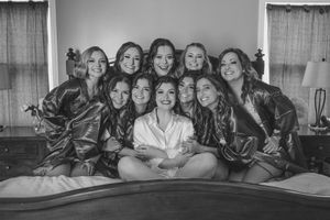 Wedding party in matching silk robes poses together on bed for group photo.