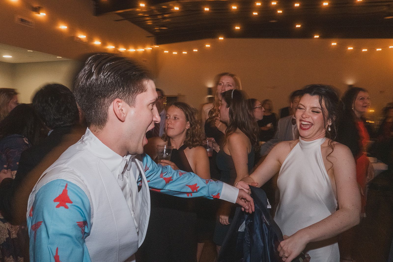 Wedding reception dance party with guests celebrating under warm string lights.