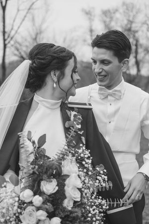 A black and white wedding photo showing a newlywed couple with a bouquet of roses and greenery in winter.