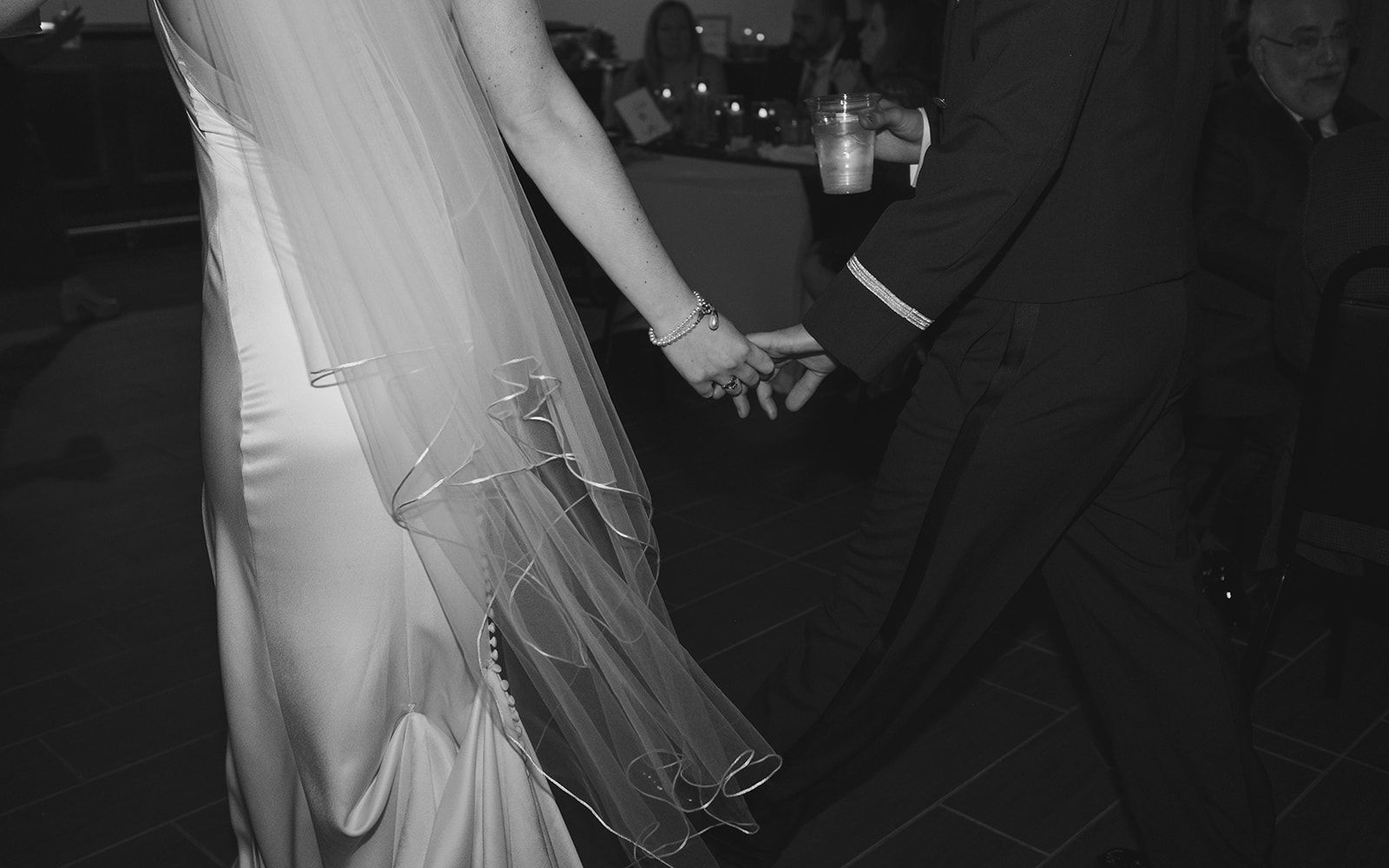 A black and white photograph shows the side of a bride's wedding dress with flowing veil during a dance.