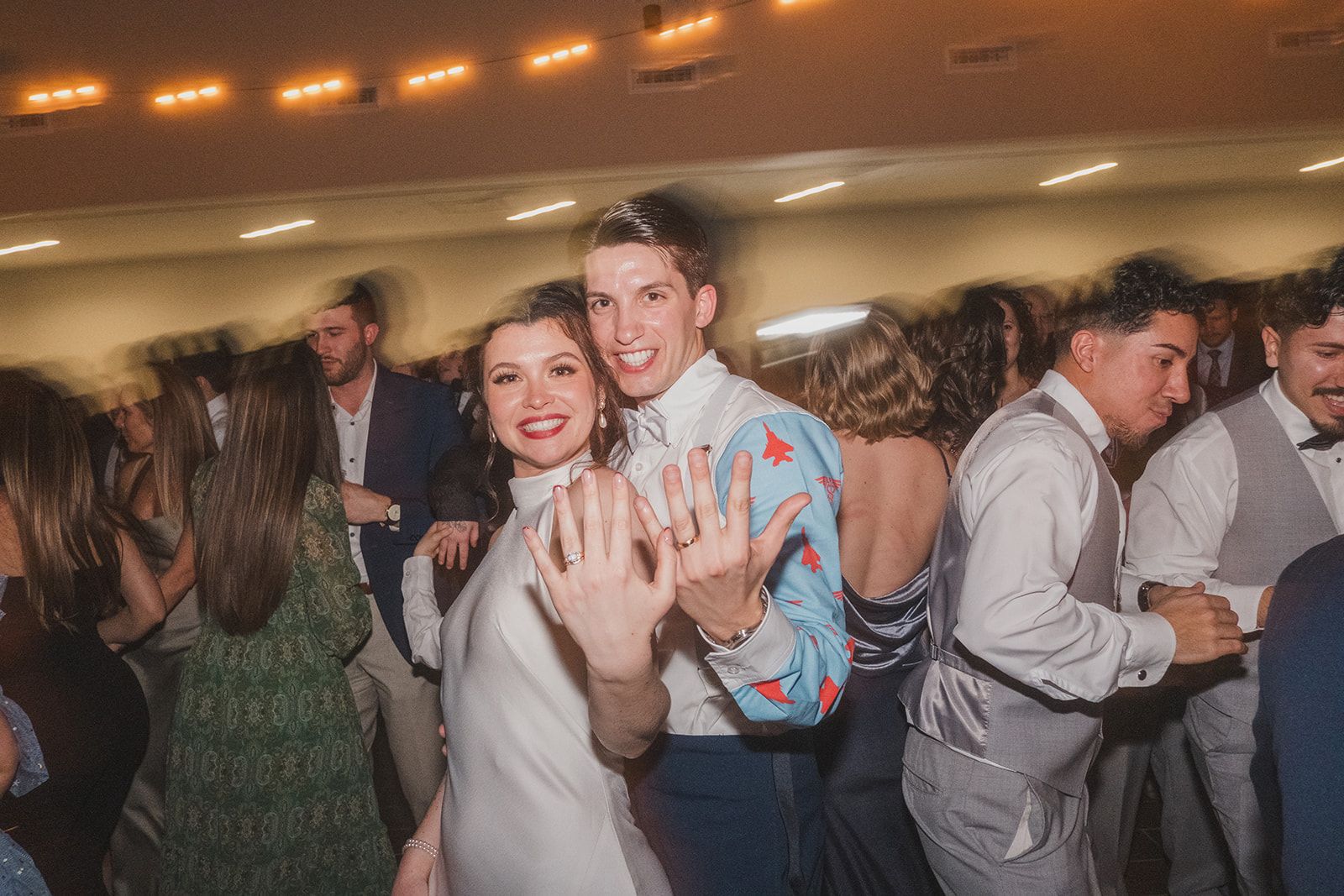Two people enjoying dancing together at a lively indoor reception with warm lighting and other guests in the background.