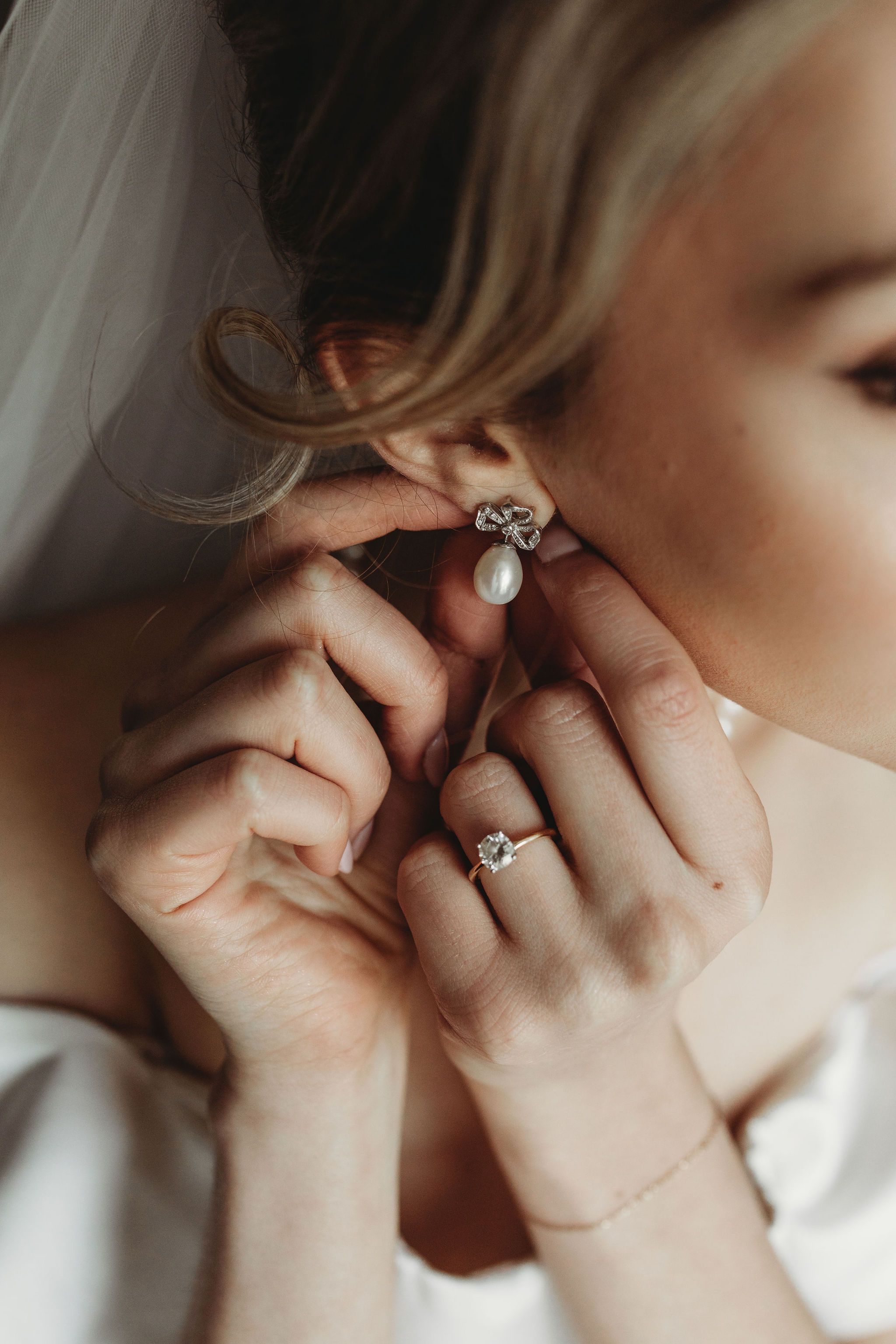 Close-up view of hands putting on an elegant pearl and crystal earring with matching ring on wedding day.