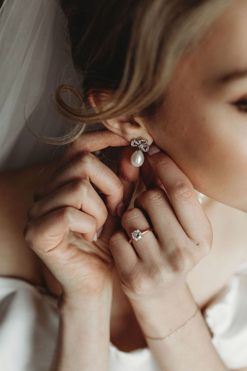 Close-up view of hands putting on an elegant pearl and crystal earring with matching ring on wedding day.