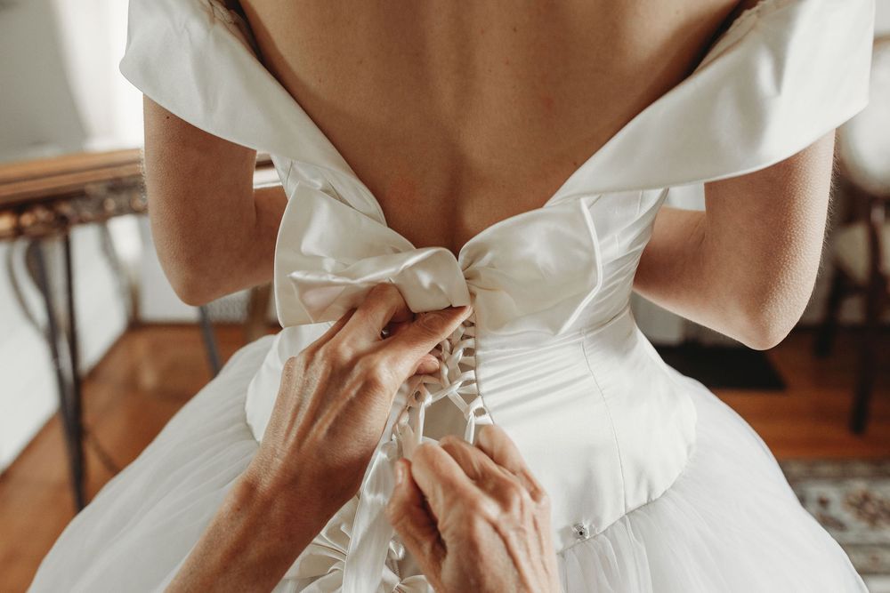 Close-up details of white bridal dress features include lace trim, buttons, and bows.