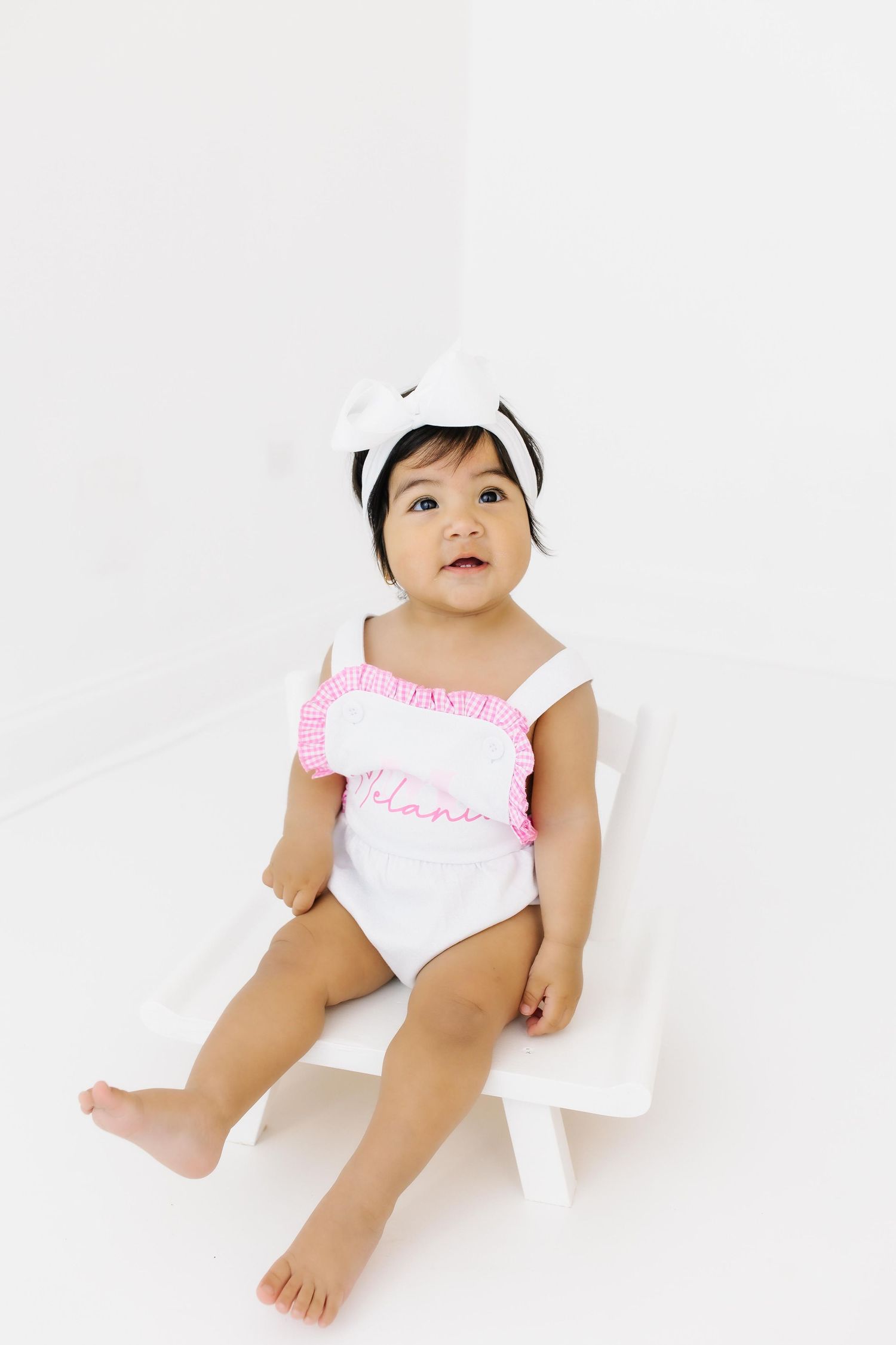 Baby in white and pink ruffled outfit lays on white background during professional photo shoot.