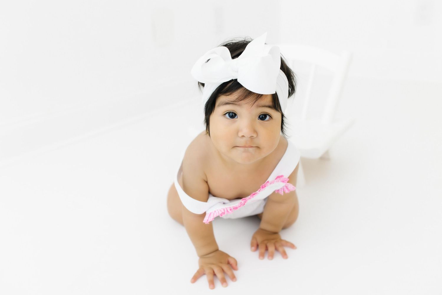 Baby in white clothing crawls and plays against a white background in a four-part collage sequence.