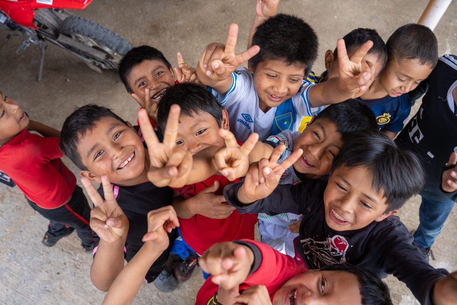 A cheerful group of kids making peace signs while smiling and looking up at the camera from below.