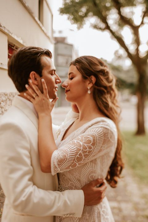 Romantic close-up of couple in elegant white wedding attire against soft outdoor backdrop.