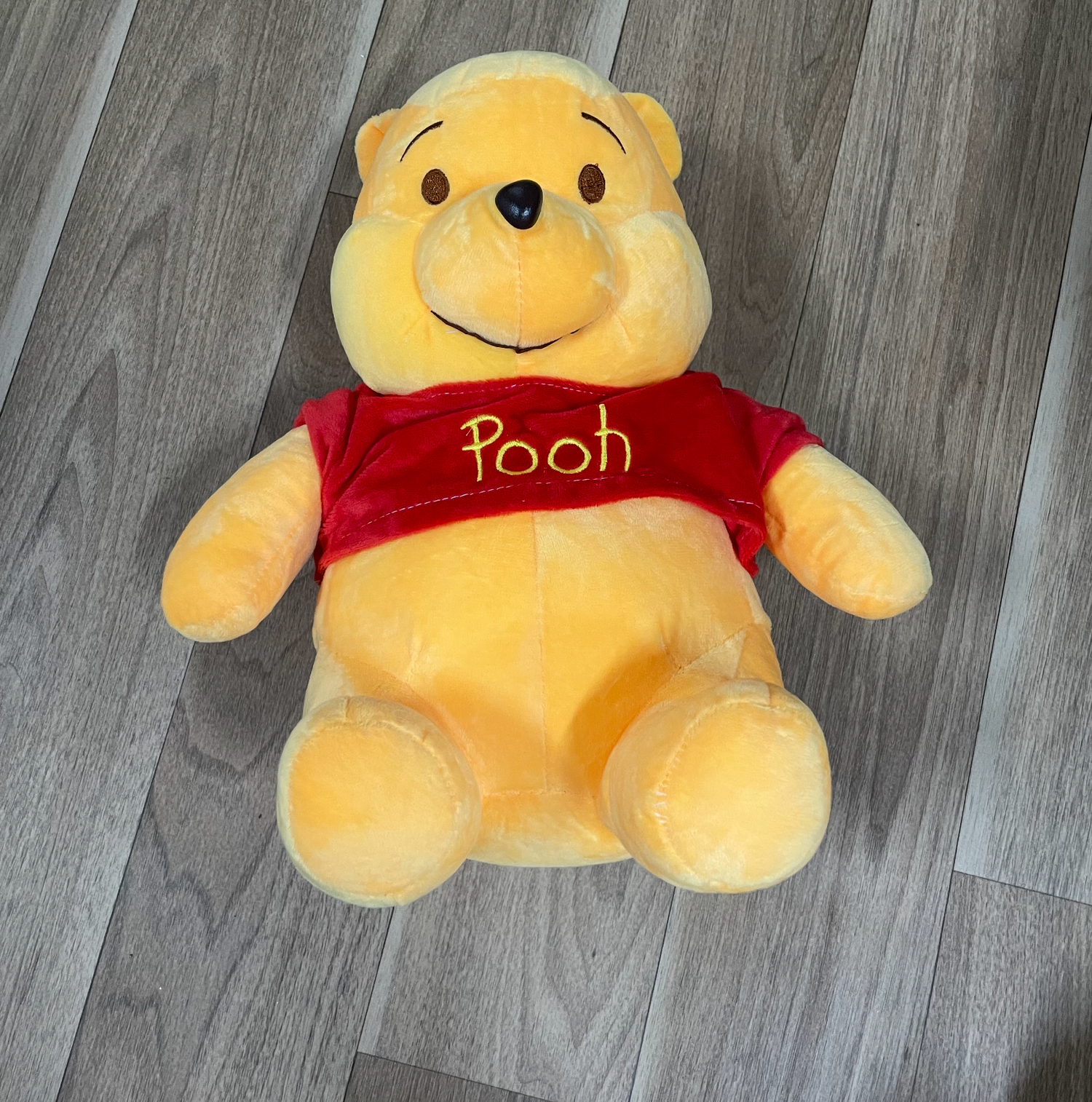 Yellow plush Winnie the Pooh bear toys arranged in sequence on wooden flooring.