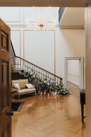 Elegant foyer with curved staircase, crystal chandelier, vintage settee and romantic floral arrangements at Rise Hall.