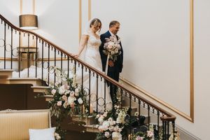 A couple descending an elegant staircase adorned with floral arrangements during a wedding celebration at Rise Hall.