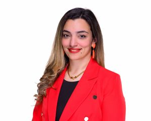 Professional woman in red blazer with orange earrings smiling against white background.